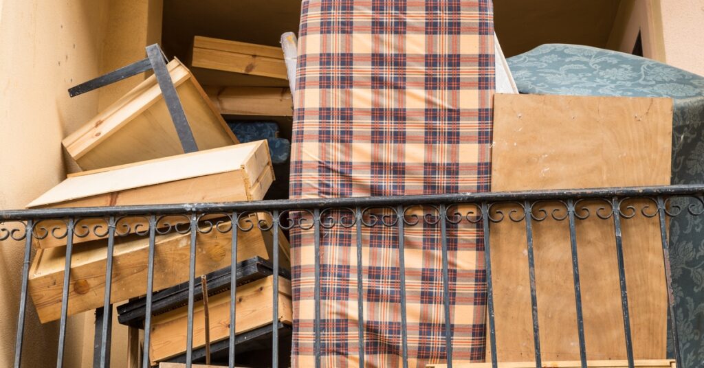 A large pile of discarded furniture, including wooden drawers, a teal couch, and a mattress, leaned against a metal railing.
