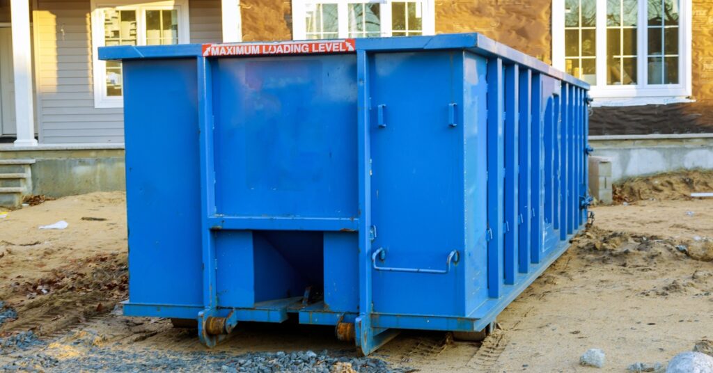 A blue roll-off dumpster in front of a home under construction on dirt. A label reads "maximum loading level" with arrows.