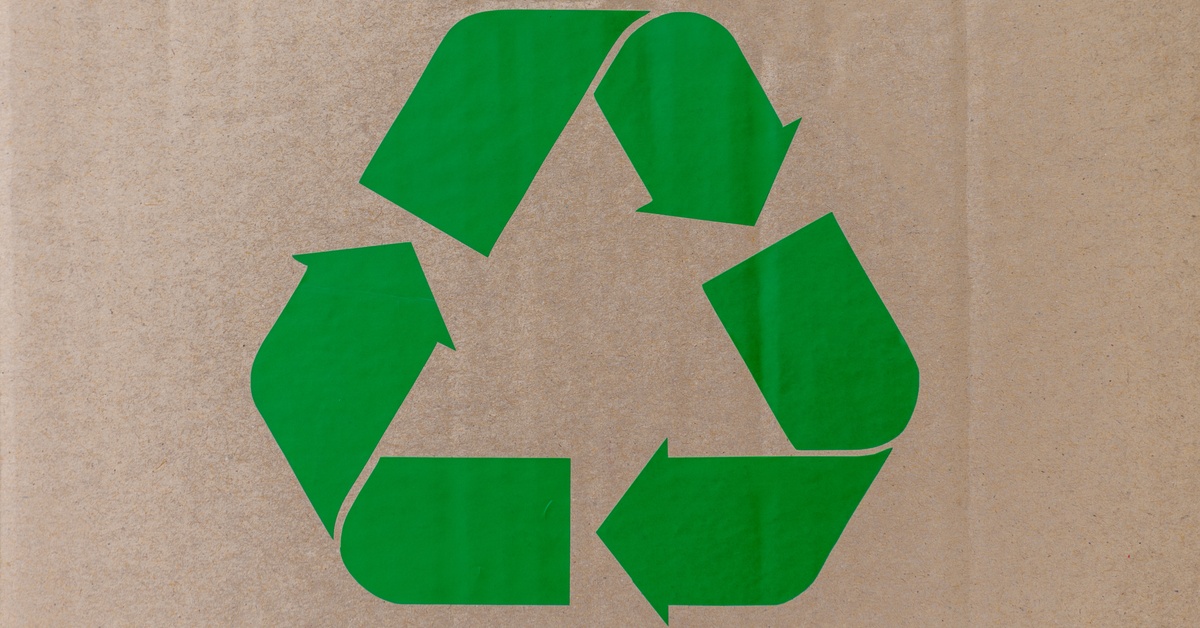 A green recycling symbol with three arrows in a triangle on a light brown cardboard background.