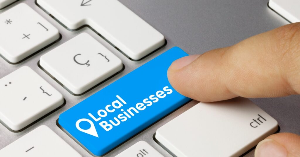 A finger presses a blue button on a Mac keyboard with a map icon and text reading "local businesses".