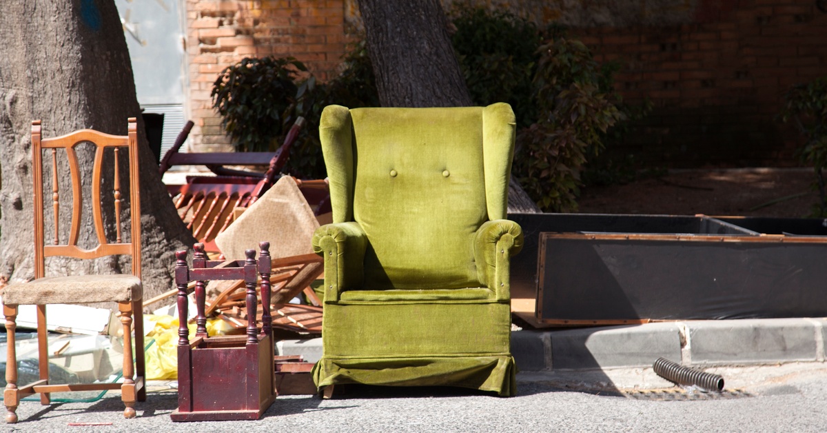 A light green accent arm chair and multiple wooden chairs sit abandoned on the corner of the street.